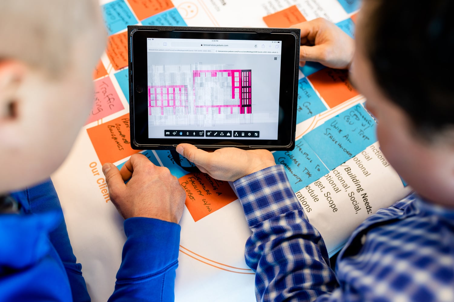 Two construction professionals reviewing a BIM model on a tablet during a collaborative design integration in construction planning session with handwritten project notes