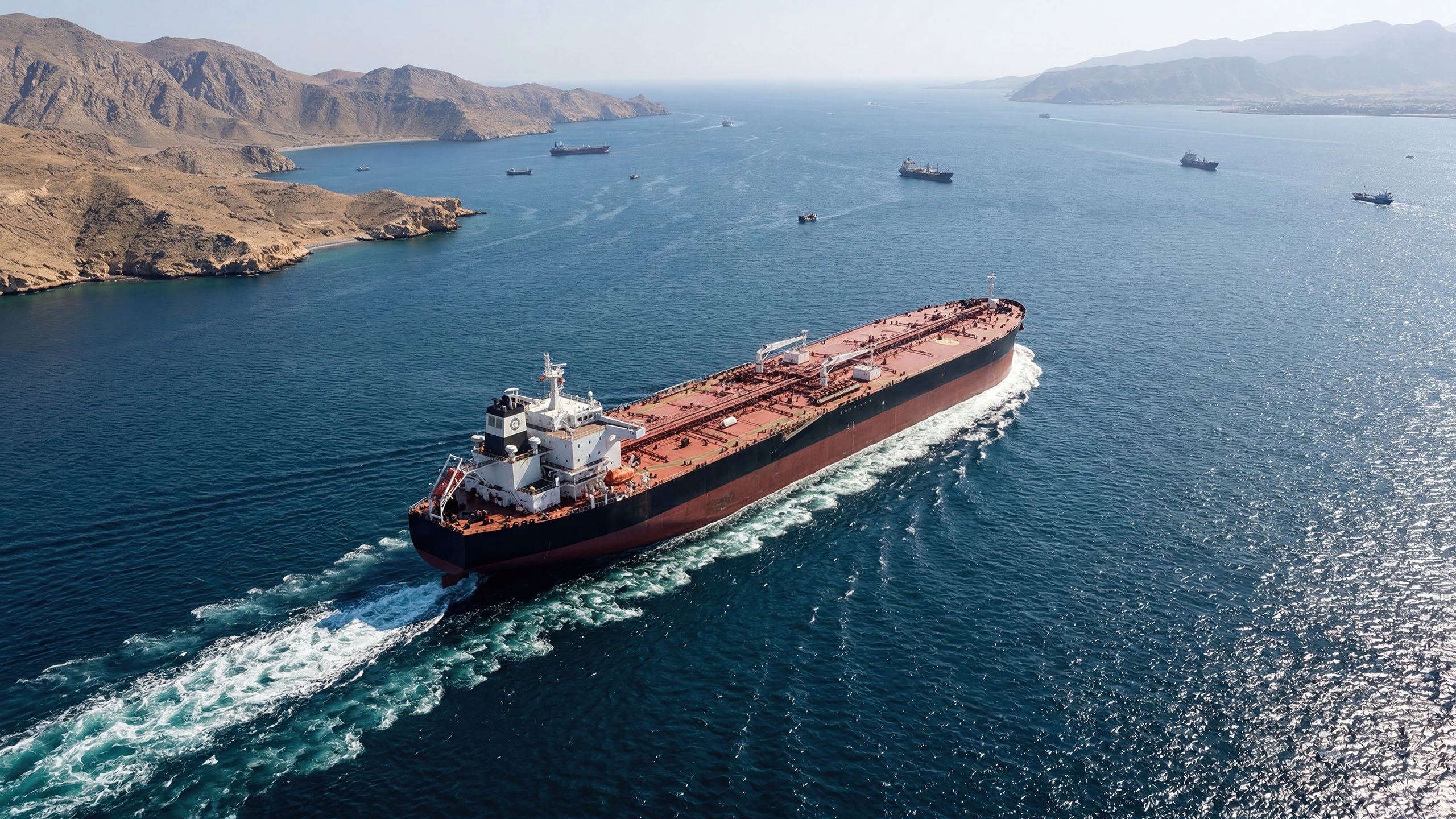 Aerial view of a crude oil tanker navigating coastal waters with other tankers anchored in the distance.
