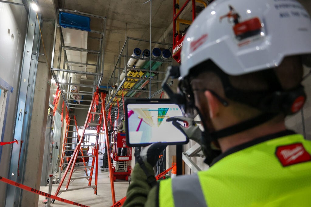 Construction professional reviews coordinated model data during prefabricated multi-trade rack installation in a laboratory utility corridor