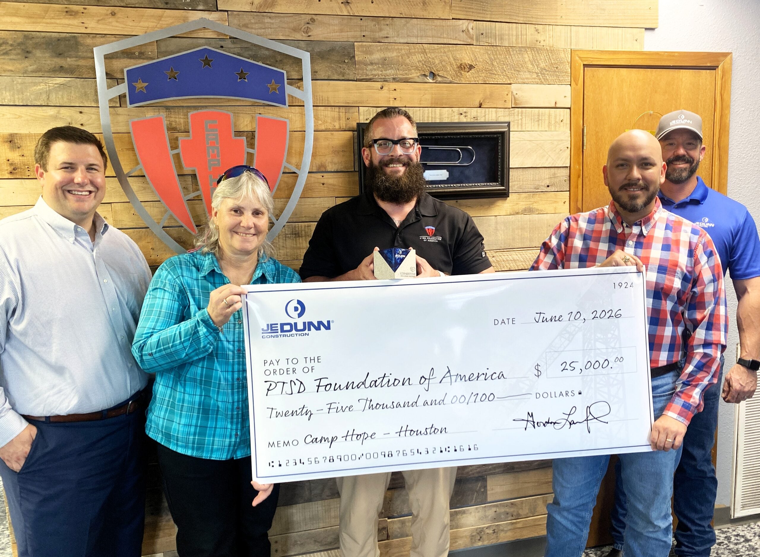 Group of five adults posing indoors, holding a large ceremonial check for $25,000 to the PTSD Foundation of America during a donation event.