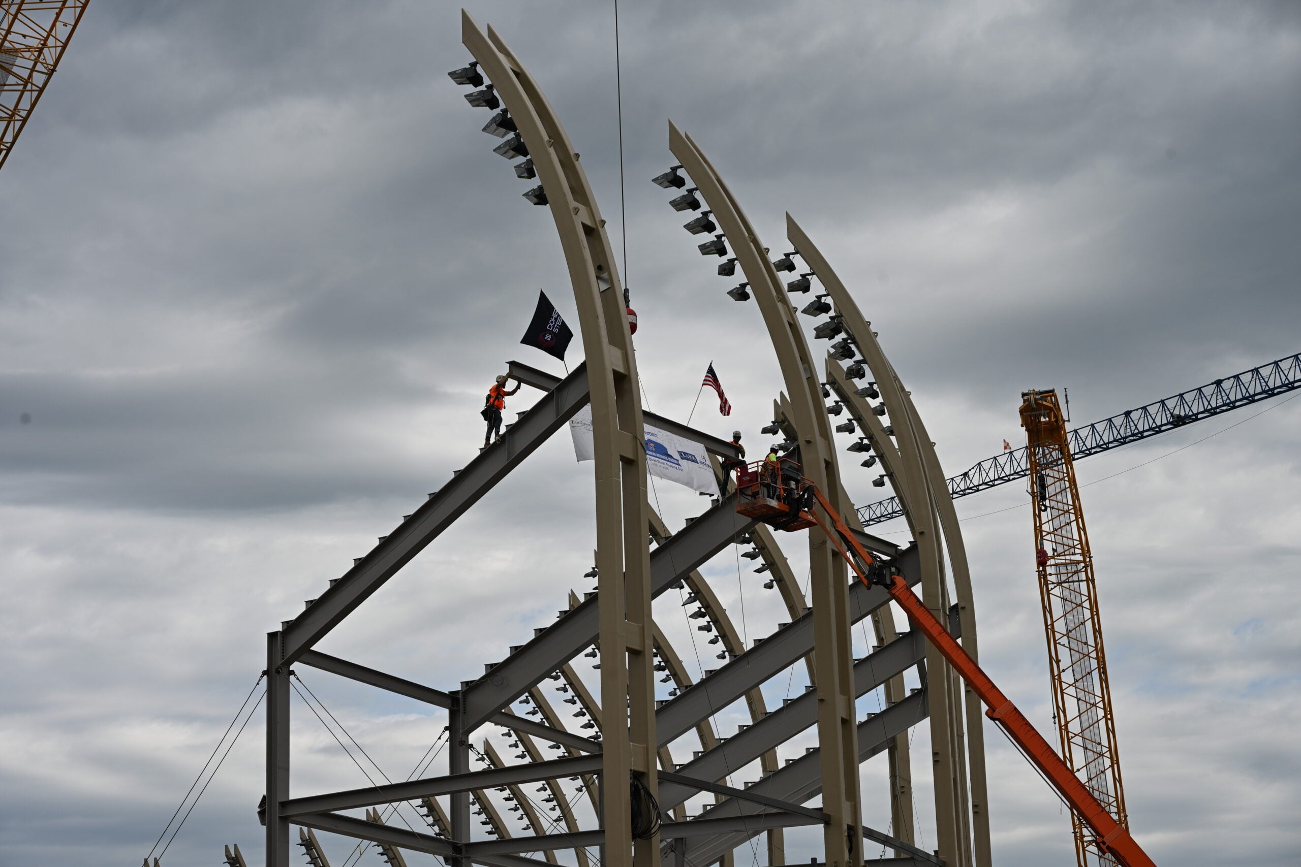 Ironworker guides final structural steel beam into place atop the KU Gateway District stadium bowl during topping out ceremony