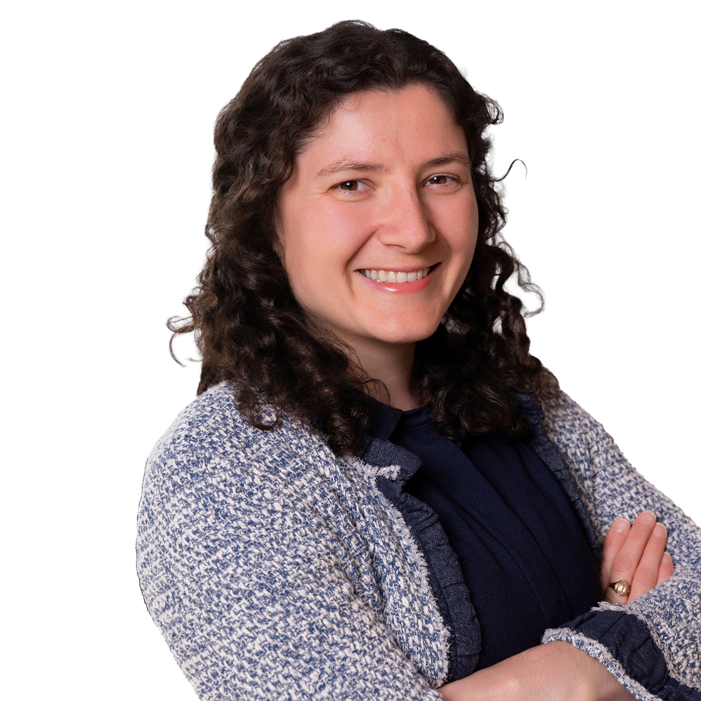 Portrait of a smiling woman with curly hair, arms crossed, wearing a navy blouse and textured light jacket.