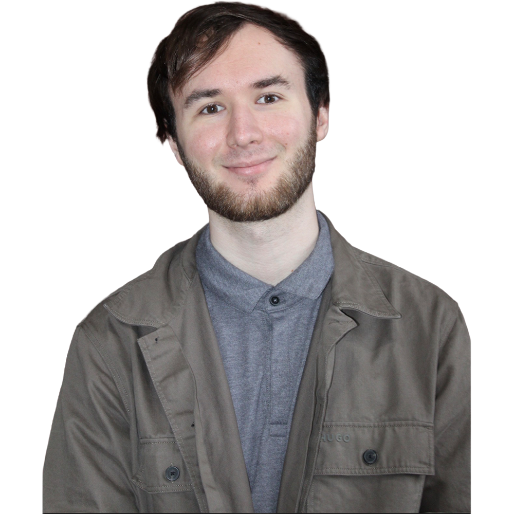 Smiling man with short dark hair and light beard wearing a gray collared shirt under a taupe jacket, posed against a neutral backdrop.