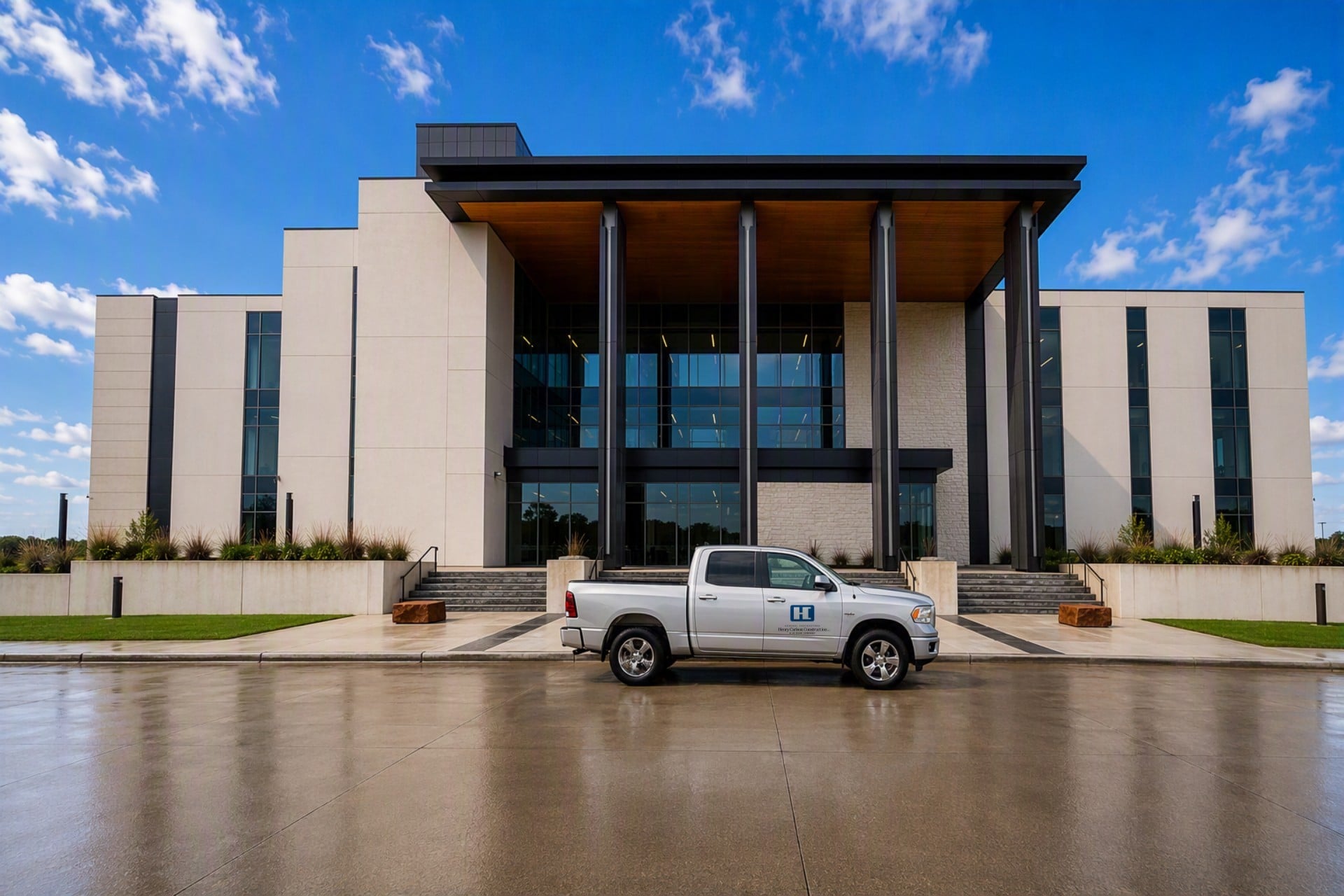 Front view of a modern office building with tall columns and glass facade; a white pickup truck is parked in front under a blue sky.