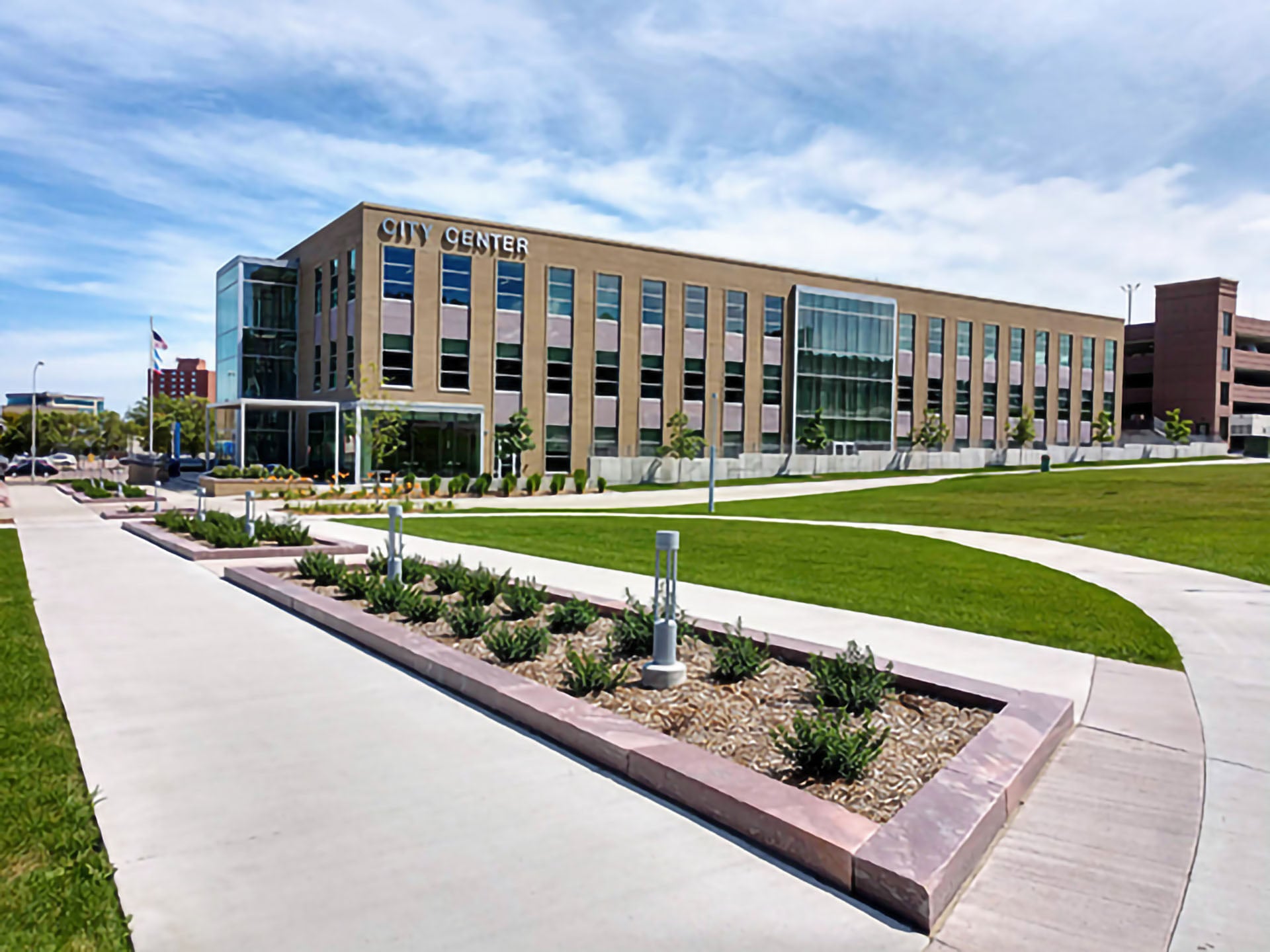 Modern brick office building labeled City Center with glass atrium and tall windows, set along curved sidewalks and landscaped planters under a blue sky.