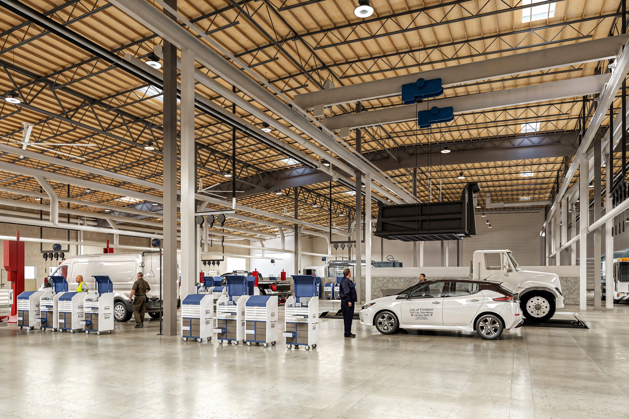 Interior of a large auto service center with vans at bays and technicians working nearby.