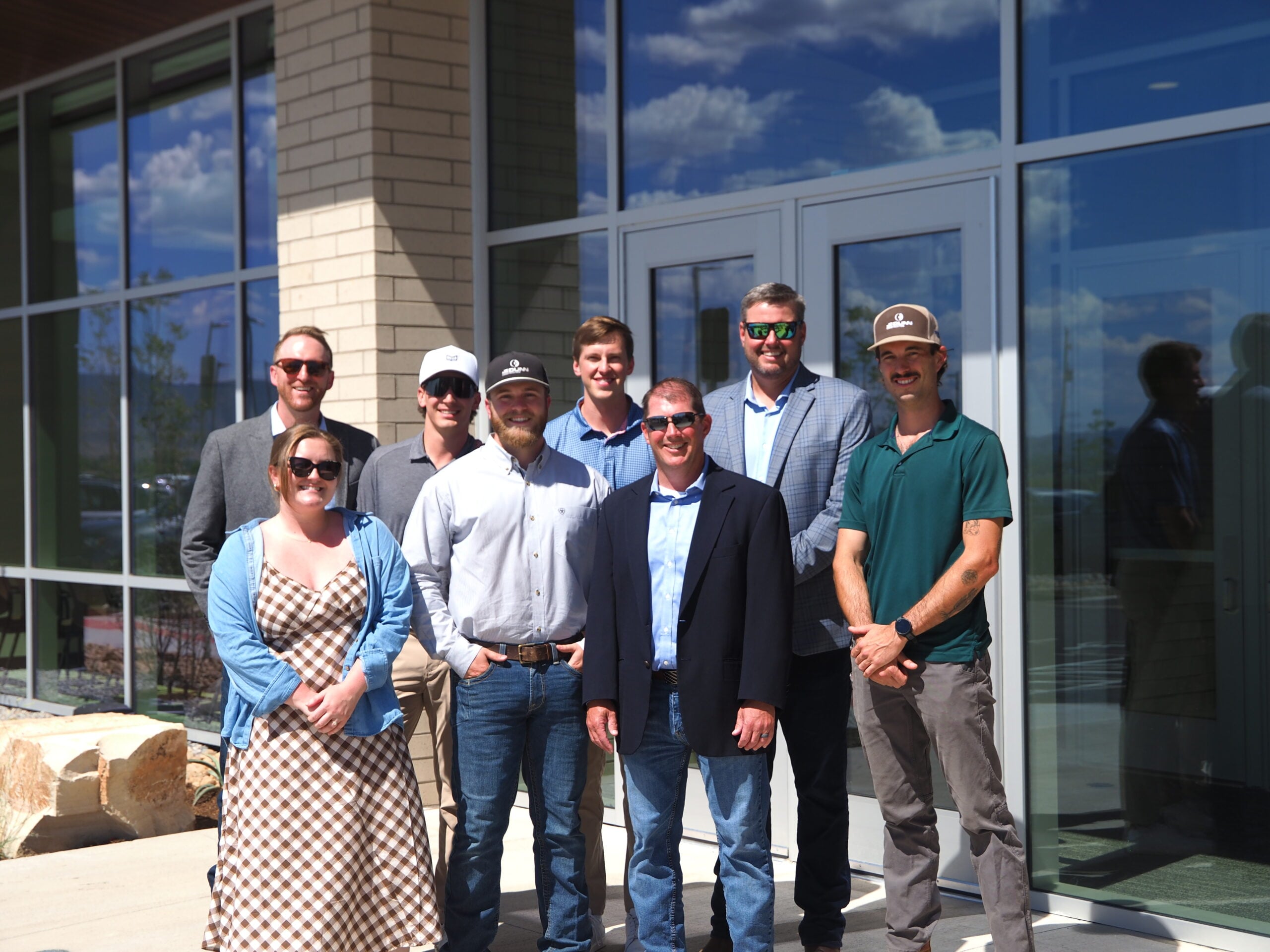 Group of professionals posing outside a glass-office building, smiling for a photo.