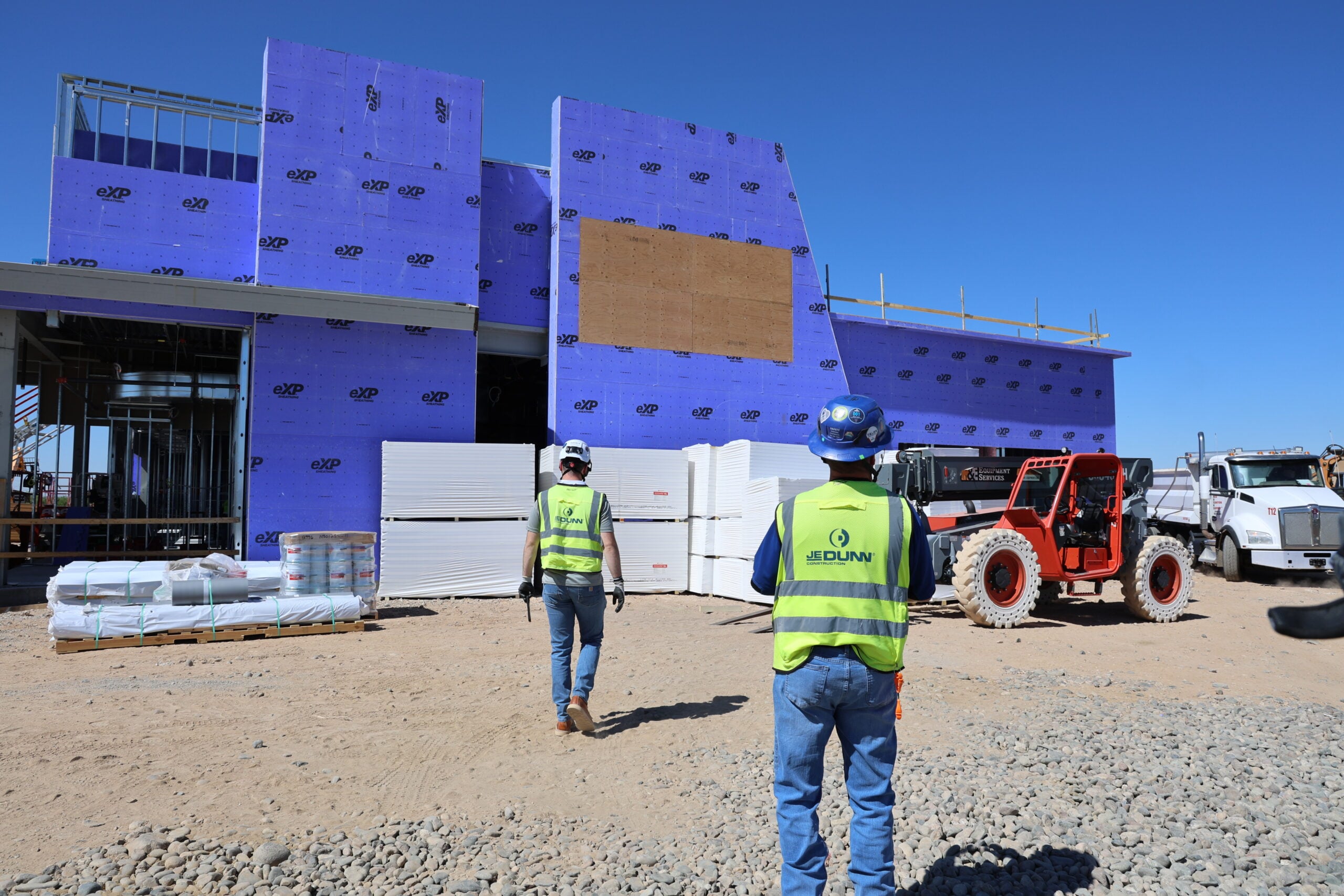 anchor health | JE Dunn Construction Construction workers in high-visibility vests observe blue exterior sheathing on a building under construction.